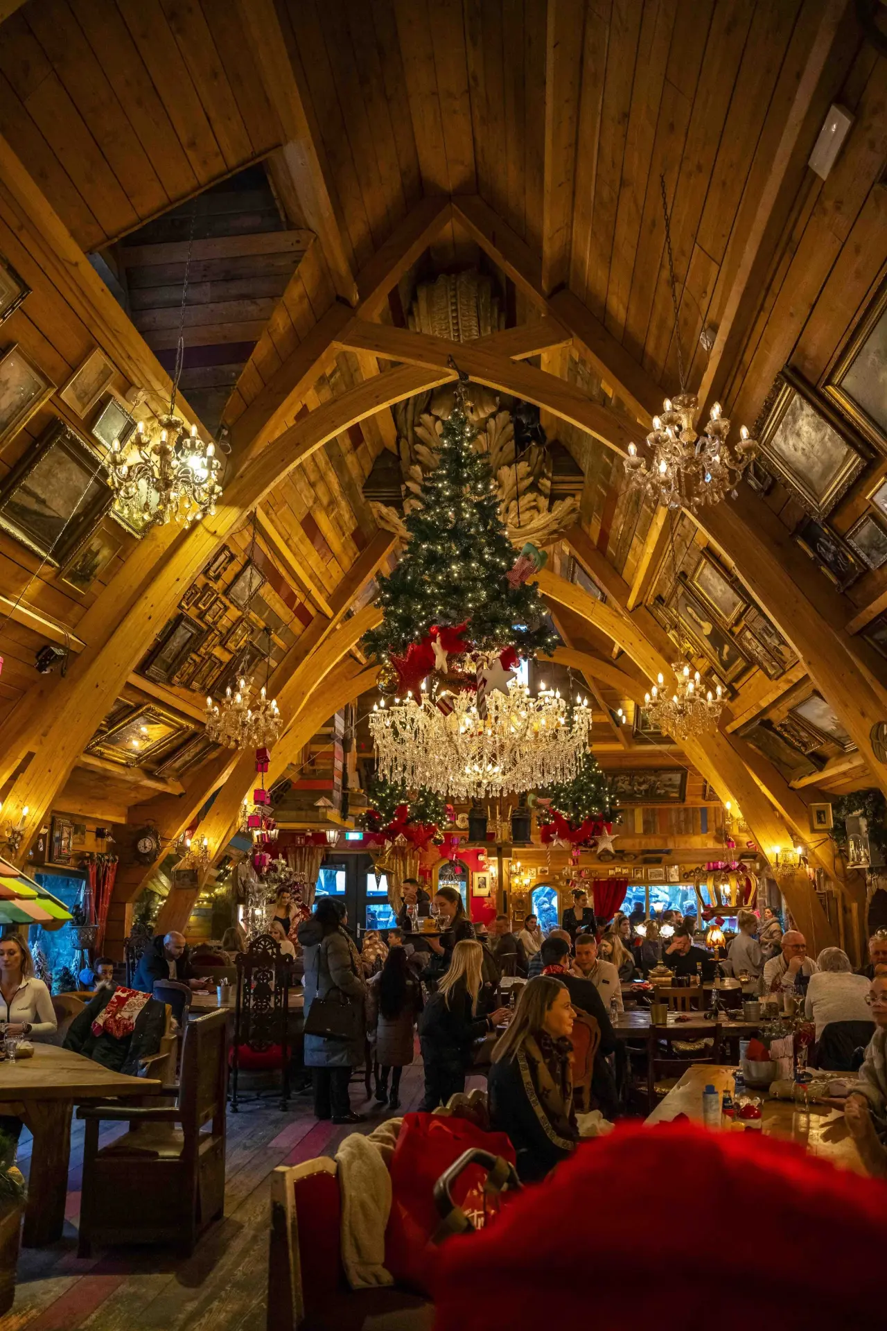 Warme houten zaal met kerstboom en kroonluchters vol gasten